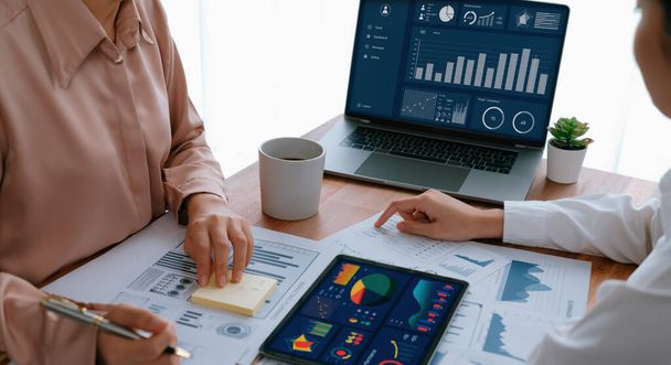 Analyst team colleague discuss financial data on digital dashboard, analyzing charts graph display on laptop and tablet screen. Modern office use business intelligence to plan marketing. Enthusiastic - Foto, Imagen