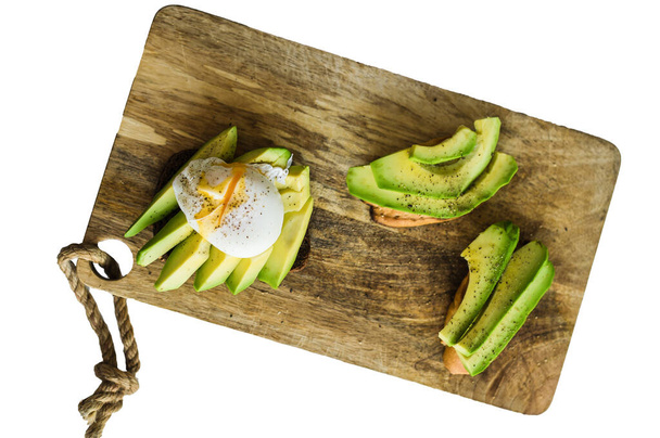 Tostadas, sándwich de avacado y huevo escalfado sobre una tabla de cortar de madera aislada sobre fondo blanco - Foto, Imagen