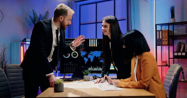 Business collaboration concept where handsome positive successful bearded businessman shaking hands with female colleagues during joint meeting in evening office - Фото, изображение