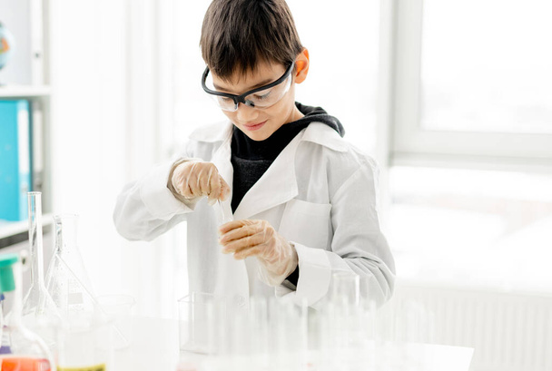 School boy wearing protection glasses doing chemistry experiment in elementary science class. Pupil with equipment tubes in lab - Foto, Imagen