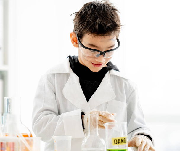 School boy wearing protection glasses with dirty face doing chemistry experiment with chemical liquids in elementary science class. Clever pupil analyzing results of test in lab - Фото, изображение