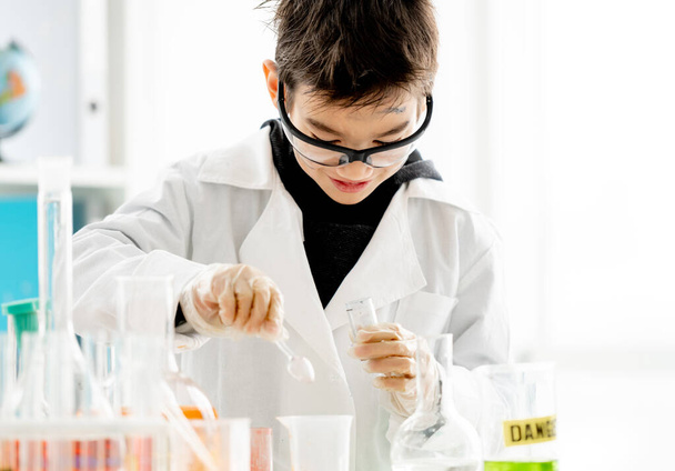 School boy wearing protection glasses with dirty face doing chemistry experiment in elementary science class and measuring components with spoon. Clever pupil in lab - Foto, Imagem