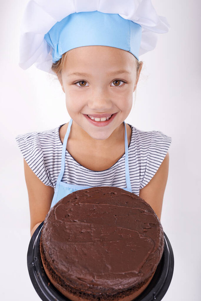 To jest smaczniejsze niż wygląda. Obraz słodkiej dziewczynki ubranej w kulinarne ubrania i trzymającej tort - Zdjęcie, obraz