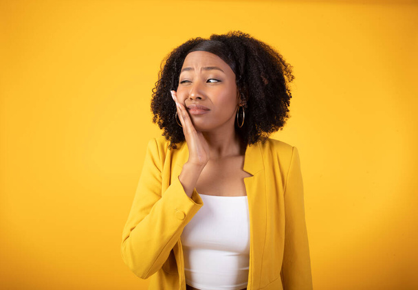Trieste jonge Afro-Amerikaanse dame in casual lijden aan kiespijn, pijn voelen en aanraken wang geïsoleerd op gele achtergrond, studio schot. Gezondheidsproblemen, tandheelkunde, cariës en gevoelige tanden - Foto, afbeelding