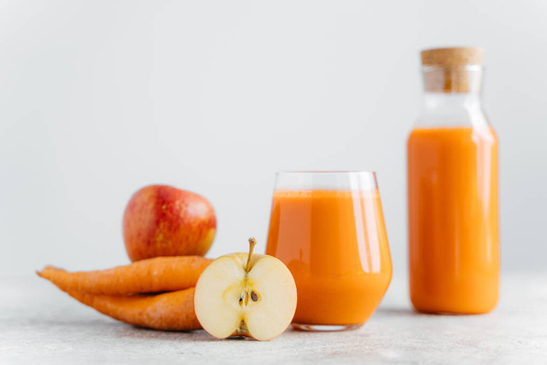 Горизонтальний знімок детоксикаційного морквяного соку в пляшці і склянці, скибочки яблука, моркви, ізольовані на білому тлі. Здоровий натуральний напій. Вибірковий фокус
 - Фото, зображення