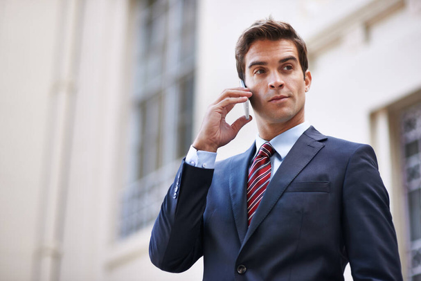 Stedelijke communicatie. Een knappe zakenman in een pak in gesprek op zijn mobiele telefoon in een stadsomgeving - Foto, afbeelding