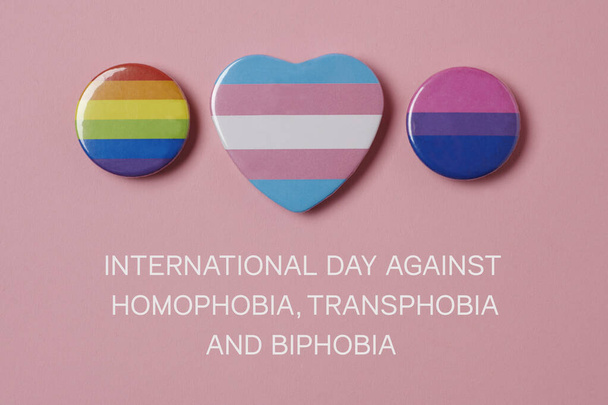 alcuni distintivi con una bandiera dell'orgoglio gay, una bandiera dell'orgoglio transgender e una bandiera dell'orgoglio bisessuale, e il testo giornata internazionale contro l'omofobia, la transfobia e la bifobia su sfondo rosa - Foto, immagini
