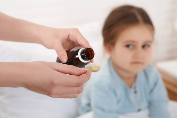 Mother pouring cough syrup into measuring spoon for her daughter indoors, focus on hands - Foto, imagen
