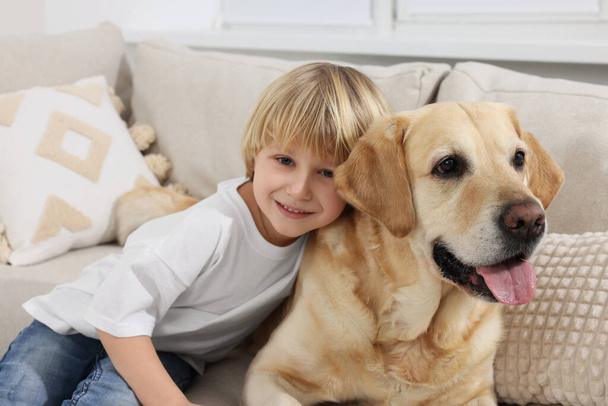 Cute little child with Golden Retriever on sofa at home. Adorable pet - Foto, Bild