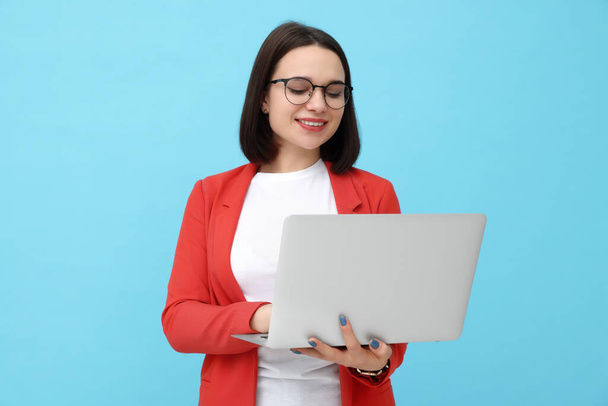 Happy young intern with laptop on light blue background - Photo, Image