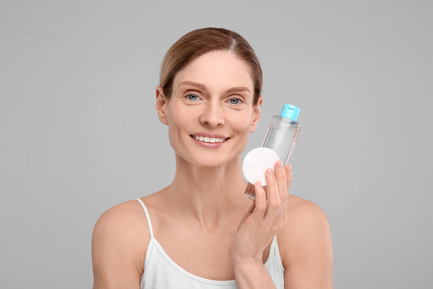 Beautiful woman with makeup remover and cotton pad on gray background - Φωτογραφία, εικόνα