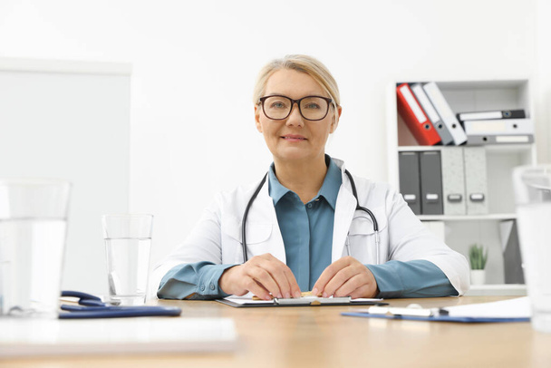 Professional doctor sitting at wooden table in clinic - Valokuva, kuva