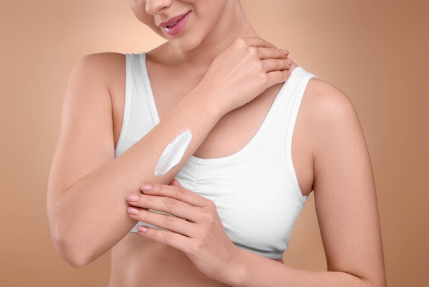 Woman with smear of body cream on her arm against light brown background, closeup - Photo, image