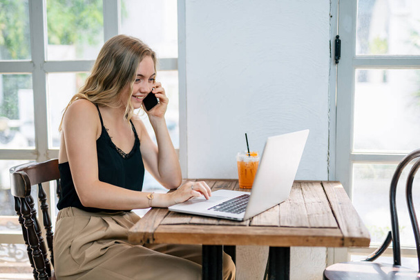 Eine freie Frau telefoniert mit Laptop am Tisch. freiberufliches Konzept. - Foto, Bild