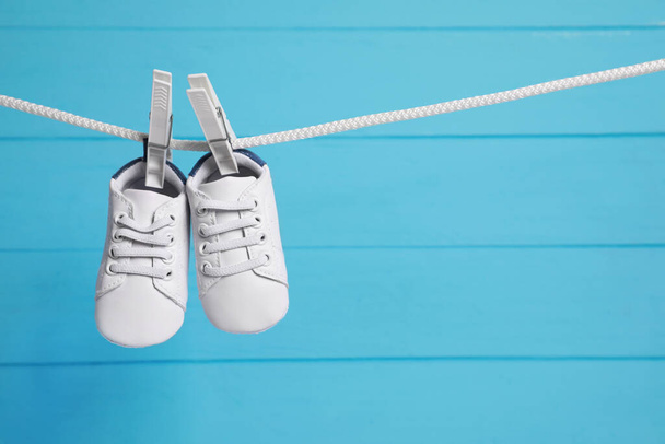 White baby shoes drying on washing line against light blue wooden wall. Space for text - Valokuva, kuva