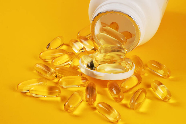 Capsule di olio di pesce con omega 3 e vitamina D in una bottiglia su giallo. - Foto, immagini