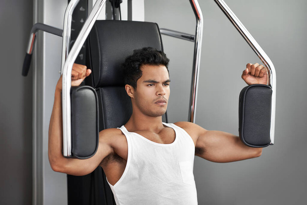Mantenerse enfocado y motivado. Un joven hombre étnico ejercitándose en el gimnasio - Foto, imagen