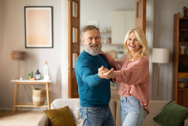 Ageless ritmus. Örömteli szerető idős házastársak ünnepli nyugdíjas élet és a szerelem egy kecses tánc otthon. Egy pár táncol és jól érzi magát a modern nappaliban. Nyugdíjba vonulás szabadidő - Fotó, kép