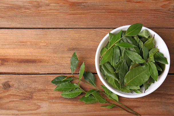 Aromatic fresh bay leaves and bowl on wooden table, flat lay. Space for text - 写真・画像