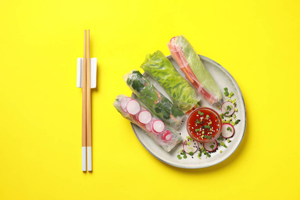 Delicious spring rolls served with sauce on yellow background, flat lay - Zdjęcie, obraz
