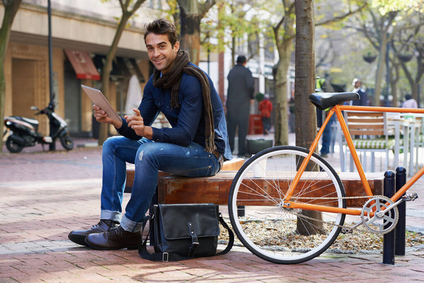 Connecting in the city. a man using his tablet while taking a break in the city with his bicycle beside him - Foto, Imagem