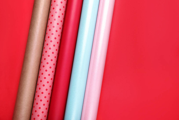 Rolls of colorful wrapping papers on red background, flat lay. Space for text - Foto, Bild