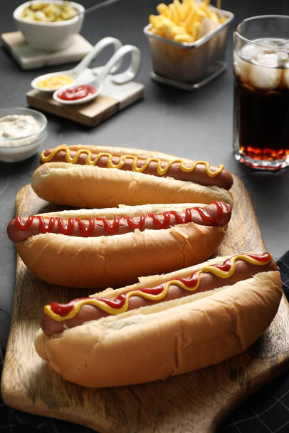 Fresh delicious hot dogs with sauces served on black table - Фото, зображення