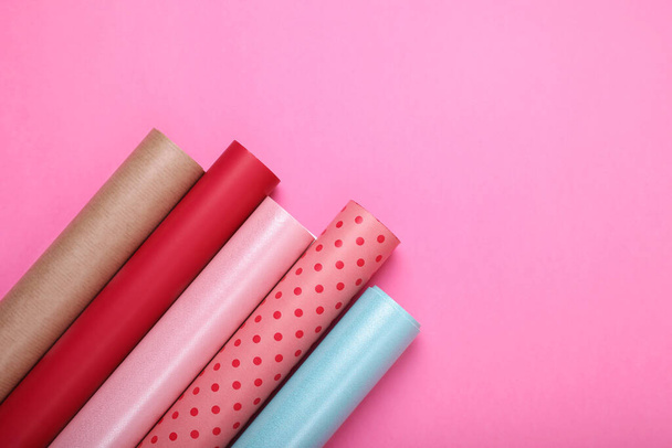 Rolls of colorful wrapping paper on pink background, flat lay. Space for text - Foto, afbeelding