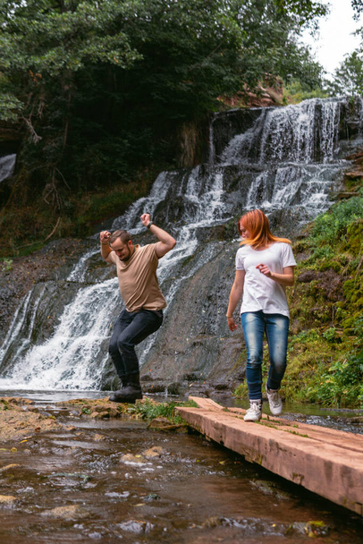 Couple having fun together outdoors on hike to amazing Dzhurynsky waterfall, Chervonogradsky waterfall. Nyrkiv, Ternopil Region, Nature of Ukraine. Vertical photo. - Zdjęcie, obraz