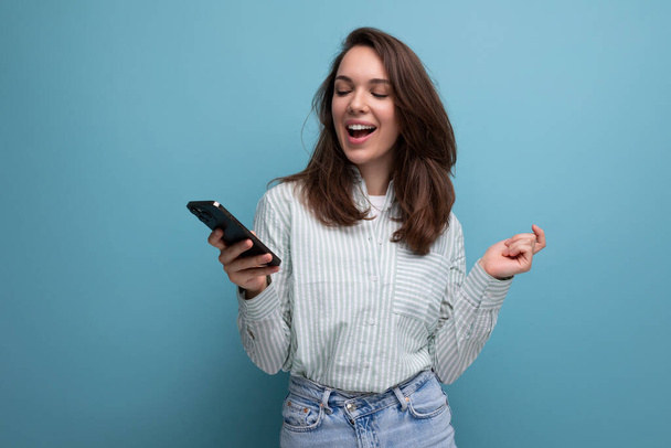 brunette jonge vrouw in shirt chatten in smartphone op studio achtergrond met kopiëren tempo. - Foto, afbeelding