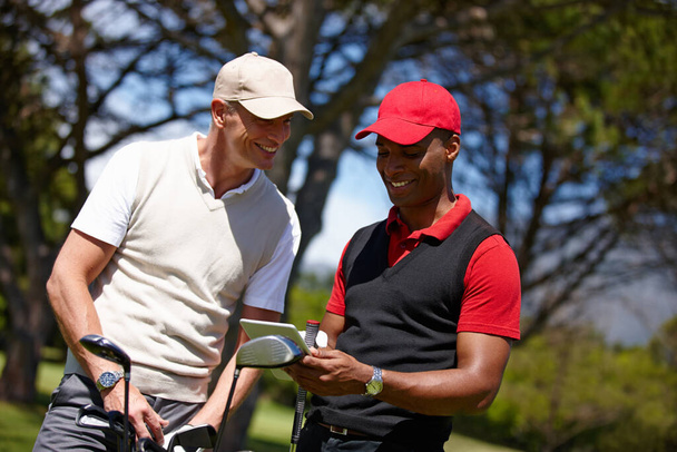 Nyomon követni a hátrányukat a technológiával. két jóképű férfi élvezi a napot a golfpályán egy digitális táblagéppel - Fotó, kép