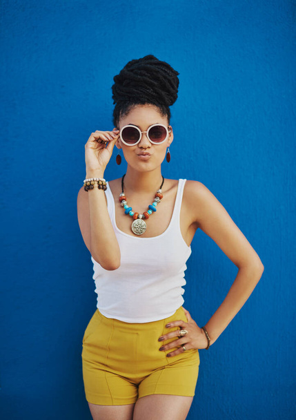 Facing the world with her funkiest look. an attractive young woman wearing funky sunglasses against a blue background - Fotografie, Obrázek