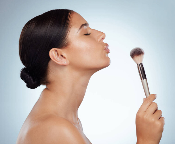 Beautiful woman holding cosmetic makeup powder brush and making kiss face. Caucasian model isolated against grey studio background and posing with copyspace. Love getting ready after skincare routine. - Fotó, kép