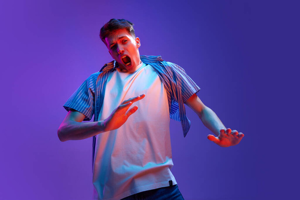 No. Portrait of young man in casual clothes showing emotions of rejection against gradient purple background in neon light. Wind blowing effect. Concept of human emotions, lifestyle, youth - Фото, зображення