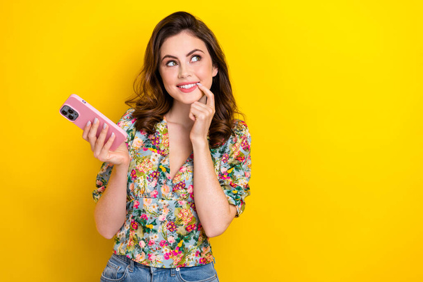 Foto van schattige minded persoon houden smart phone vinger aanraking lip look lege ruimte geïsoleerd op gele kleur achtergrond. - Foto, afbeelding