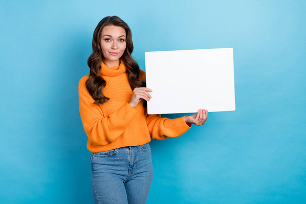 Photo of funny positive lady dressed orange pullover holding white placard emtpy space isolated blue color background. - Photo, Image