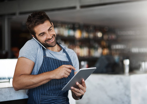 O fornecedor dele sabe do que gosta. um jovem usando um tablet digital e telefone celular enquanto trabalhava em um café - Foto, Imagem