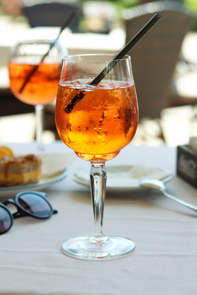 A glass of aperol spritz or campari orange cocktail with orange slice and ice on a restaurant table on the seashore on a sunny day. Holiday concept. Summer cocktails, live photo in vacation - Photo, Image