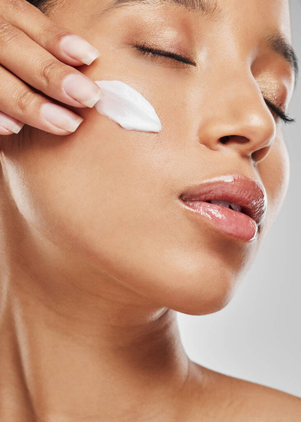 Moisturising reduces the chances of skin problems. Studio shot of an attractive young woman applying moisturiser on her face against a grey background - Photo, Image