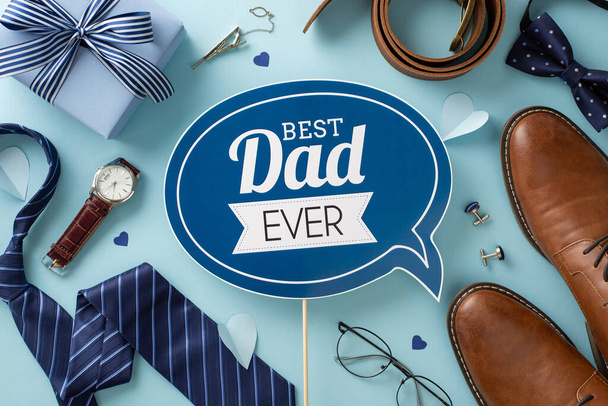 Trendy Father's Day concept. Flat lay of greeting plaque, gift box, leather shoes, necktie, bow-tie, wristwatch, accessories, belt, cufflinks, spectacles on blue background - Photo, Image