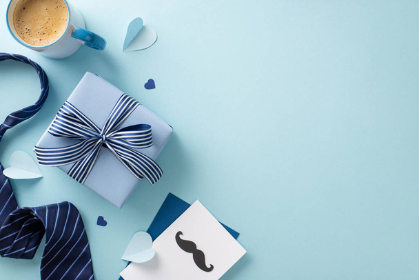 Fashionable Father's Day layout. Top view of envelope, postcard with mustaches, gift box, necktie, paper hearts, accessories, coffee mug on blue surface with space for copy - Photo, Image