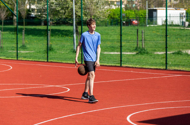 Мальчик играет в баскетбол на площадке. Подросток бегает по стадиону. Спорт, хобби, активный образ жизни для мальчиков - Фото, изображение