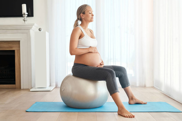 Manteniendo sus músculos en forma para el parto. una mujer embarazada haciendo ejercicio con una pelota de ejercicio en casa - Foto, Imagen