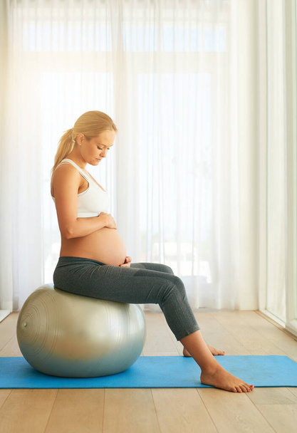 Keeping herself and her baby in good health. a pregnant woman working out with an exercise ball at home - Фото, зображення