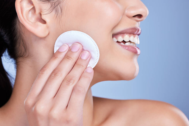 A beautiful smiling mixed race woman using a cotton pad to remove makeup during a selfcare grooming routine. Hispanic woman applying cleanser to her face against blue copyspace background. - Photo, Image