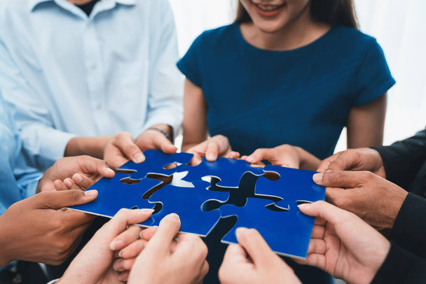 Diverse corporate officer workers collaborate in office, connecting puzzle pieces to represent partnership and teamwork. Unity and synergy in business concept by merging jigsaw puzzle. Concord - Photo, Image