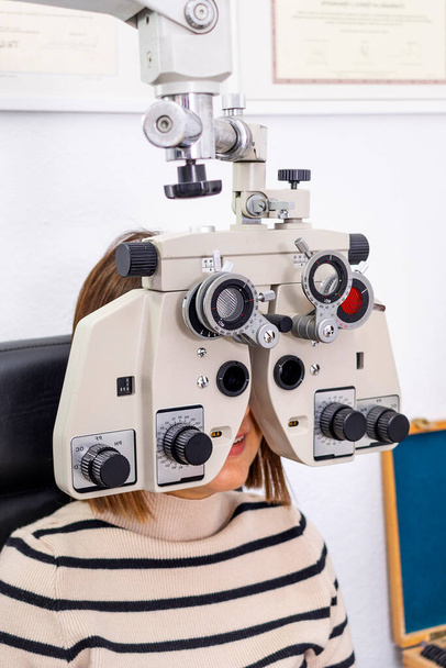 Óptico y optometrista. Mujer joven durante una prueba visual con foropter. - Foto, imagen