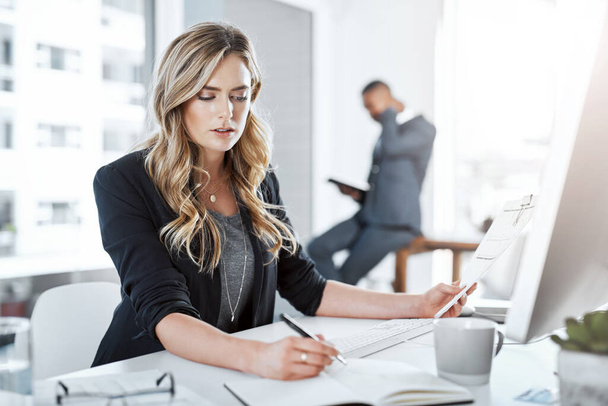O sucesso é um cinch quando você é um multitasker. uma jovem empresária usando um computador e escrevendo notas em sua mesa em um escritório moderno - Foto, Imagem