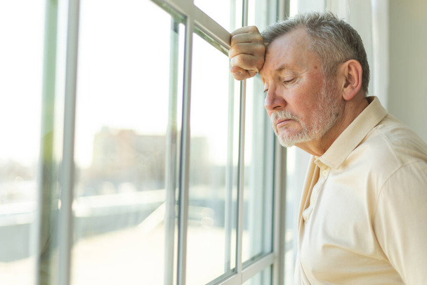 Λυπημένος κουρασμένος μοναχικός απογοητευμένος ηλικιωμένος άνδρας στο σπίτι μόνος. Δυστυχισμένος παππούς κοιτάζοντας δυστυχώς έξω από το παράθυρο βιώνει θλίψη σχετικά με το θάνατο άσχημα νέα. Στρεσαρισμένος ηλικιωμένος που υποφέρει από μοναξιά - Φωτογραφία, εικόνα
