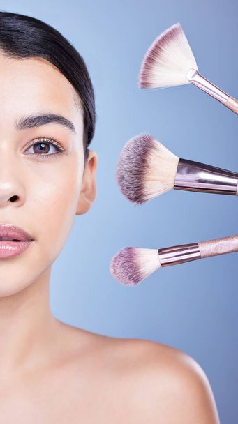 Studio Portrait of a beautiful mixed race woman posing with a collection of makeup brushes during pamper routine. Hispanic model with cosmetic tools standing against a blue copyspace background. - Photo, image